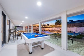 Chill and play! Covered patio with pool table, outdoor dining, and yard views perfect for evening hangouts.