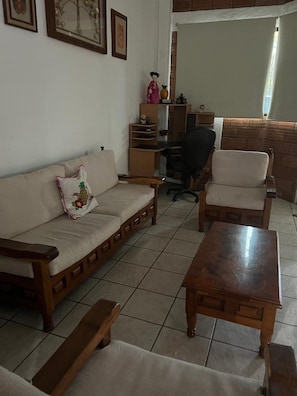 Sala (vista desde el sillón, mesa de centro, escritorio con silla de oficina, cuadros decorativos, sillón, persianas)