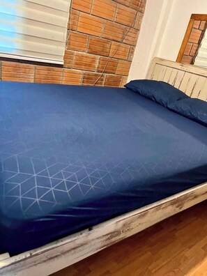Habitación (vista desde la cama, pared de ladrillos, ventana con persiana, cabecera de madera, espejo)