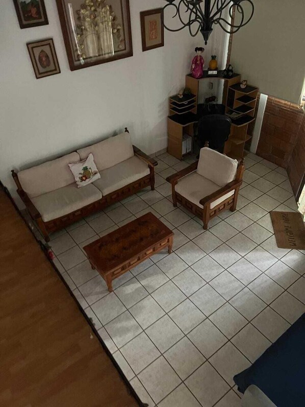 Sala (vista desde arriba, sofá, sillón, mesa de centro, escritorio con silla, cuadros en la pared)