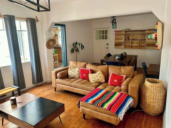 Sala (sofá, mesa de centro, banco largo, planta, sombreros de decoración, focos, lámpara, escritorio con silla, mesa con 4 sillas, cantina, cortinero)