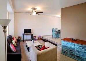 Sala (Vista desde la esquina de la tv, sofá cama, sillón individual, ventana, televisión, mueble para televisión, mesa de centro mármol)