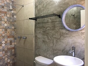 Baño (visto desde la ducha, lavabo, taza de baño, espejo redondo, toallero, pared con azulejos decorativos)
