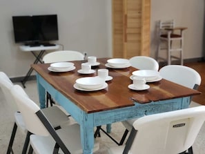 Comedor (visto desde la mesa de madera, sillas blancas, televisor)