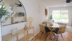 Bright and welcoming dining area complemented by a nearby mirror that enhances the natural light from the window and offers a spacious feel into the connected living space.
