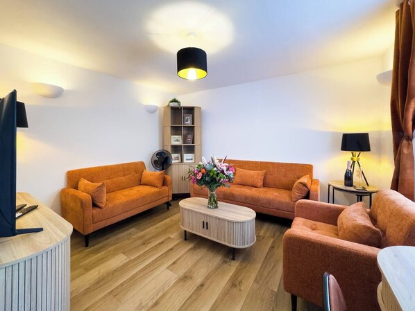 Stylish Social Lounge – This inviting space boasts bold burnt-orange sofas, warm wooden flooring, a Smart TV with Sky, and colourful accents that brighten the space.