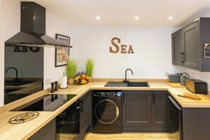 Modern Kitchen with Rustic Flair – A fully equipped kitchen with sleek black cabinets, wooden worktops, and playful coastal wall décor.