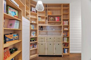 Chic ground-level hallway showcasing an open cabinet filled with reading materials, board games, and toys — the perfect blend of style and family-friendly fun.
