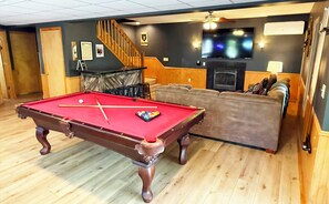 The1st floor game room features a sofa, 75" TV, fireplace, pool & shuffleboard.