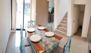 Cocina (vista desde la sala, cocina, mesa con sillas, escaleras, puerta del baño, entrada a la casa)