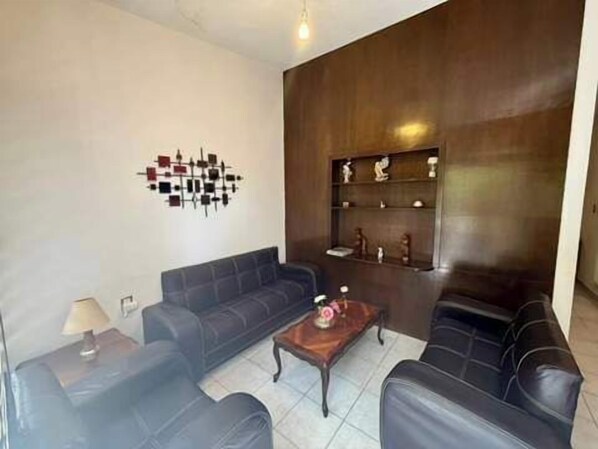 (sillones negros, mesa central con adornos, mueble con repisas y adornos, decoración en la pared, mesa de madera con lampara de noche)