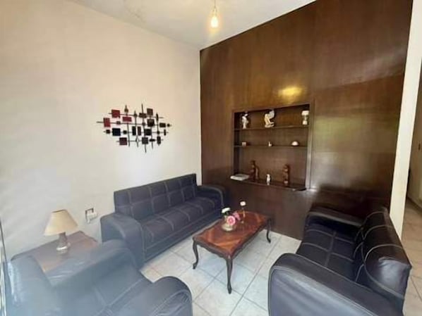 (sillones negros, mesa central con adornos, mueble con repisas y adornos, decoración en la pared, mesa de madera con lampara de noche)