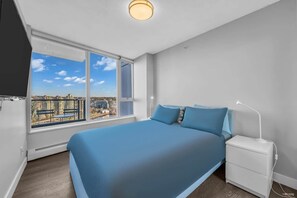 Tranquil and inviting, this bedroom features a plush bed dressed in calming blue tones, large windows offering breathtaking city views, and sleek, minimalist furnishings for a peaceful retreat.