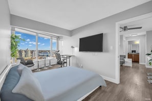 Wake up to panoramic city views in this airy bedroom, featuring a comfortable bed, a wall-mounted TV, and a versatile workspace that seamlessly blends relaxation and productivity.