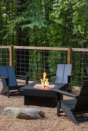 Outdoor fire pit lounge surrounded by forest greenery.