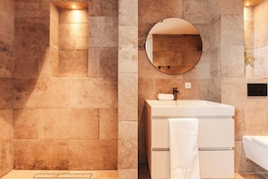 A stylish bathroom with natural stone walls, featuring a modern vanity, circular mirror, and soft lighting. The minimalistic design and textures create a serene and elegant atmosphere.
