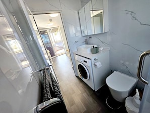 Fully functioning bathroom with toilet, shower, hand basin, mirror vanity and washing machine.