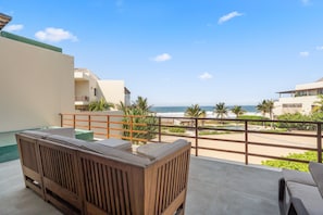 The terrace seamlessly extends from the indoor living area, offering a front-row view of the sea and lush palm trees.