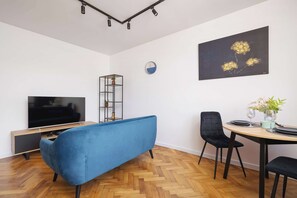 A small living and dining area with a turquoise sofa, TV, and a dining table with two chairs. Wooden flooring adds warmth to the space.
