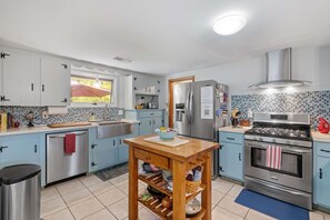 Channel your inner chef in this bright kitchen featuring a stainless steel farmhouse sink, gas stove, and custom backsplash full of coastal color.