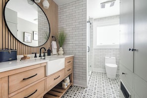 This luxurious bathroom features beautiful tile, a spacious vanity with farmhouse style sink and a roomy walk in shower