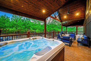 Covered deck features private hot tub, forest backdrop, and evening-ready lighting.