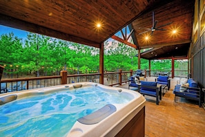 Covered deck features private hot tub, forest backdrop, and evening-ready lighting.