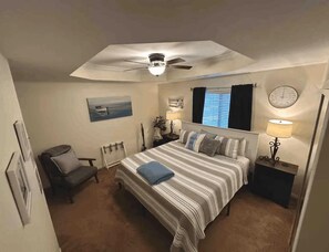 This inviting bedroom features a comfortable queen-sized bed, a ceiling fan, and tasteful decor, including a serene boat painting above the headboard, ensuring a relaxing stay.