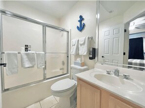 Clean and functional bathroom with a shower, vanity, and a charming nautical anchor decoration, stocked with fresh towels and essential toiletries for your convenience.