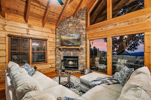 Let laughter and love fill our cabin's inviting living room, complete with a cozy fireplace, floor-to-ceiling windows, and ample space for family fun