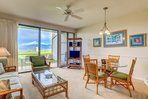 NAP-B43 The bright and airy living room features tropical decor, cozy seating, and panoramic windows showcasing the outdoor beauty of Hawaii.