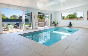 Piscine intérieure chauffée offrant une vue panoramique sur le jacuzzi extérieur et la terrasse aménagée.