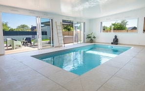 Piscine intérieure chauffée offrant une vue panoramique sur le jacuzzi extérieur et la terrasse aménagée.