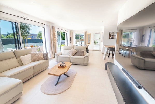 Grand salon familiale avec salon TV HD 98" vu sur la terrasse et le jardin