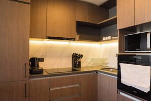 Sleek and modern kitchen with all essentials for a comfortable stay, featuring stylish wooden cabinetry and ambient lighting.