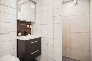 Functional Bathroom Space – Practical layout with large mirror, storage drawers, and tiled walls.