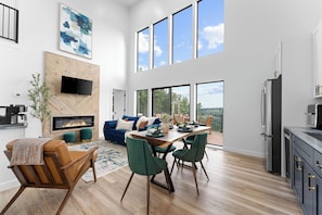 Stunning open-concept living area with soaring ceilings, modern fireplace, and floor-to-ceiling windows offering breathtaking Ozark views. This stylish family vacation home in Branson is minutes from Silver Dollar City, Table Rock Lake, and more!