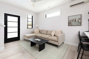 Relax in this stylish, sunlit living room featuring a cozy sectional, sleek décor, and plenty of natural light.