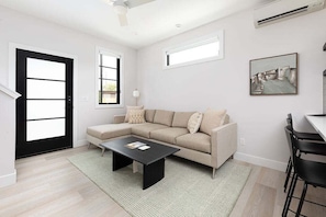 Relax in this stylish, sunlit living room featuring a cozy sectional, sleek décor, and plenty of natural light.