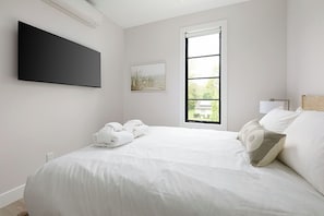Bedroom 2 offers a comfortable queen bed, natural light, and thoughtful touches like bedside lamps and fresh towels.