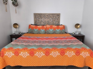 The inviting bedroom boasts a colorful queen bed with elegant nightstands, creating a warm and relaxing retreat.
