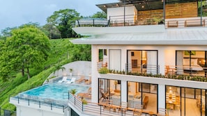 This multi-level home glows at twilight with lit terraces, a sparkling infinity pool, and outdoor loungers.