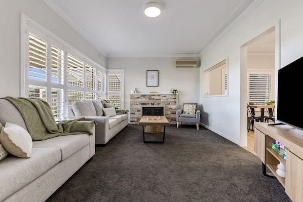 Light-filled living room with flat screen TV, seating area & split-system air-conditioner.