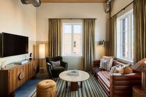 TV lounge with brown sofa, round table, and sunny window view