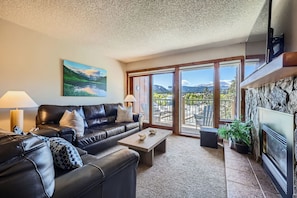 Cozy up in this inviting living room with plush leather seating, a warm stone fireplace, and stunning mountain views right from your private balcony.