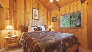 Primary bedroom with a California King size bed, plush bedding, smart TV, and peaceful forest views