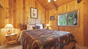 Primary bedroom with a California King size bed, plush bedding, smart TV, and peaceful forest views