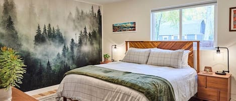Spacious primary bedroom with King size mattress and forest wallpaper.