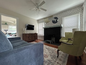 Comfy coastal living room with pull out couch, smart TV & ceiling fan.