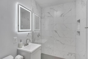Stylish bathroom with walk-in shower and LED mirror.
